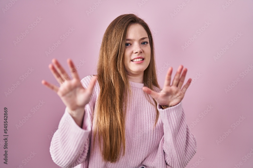 Young caucasian woman standing over pink background afraid and terrified with fear expression stop gesture with hands, shouting in shock. panic concept. Young caucasian woman standing over pink background afraid and terrified with fear expression stop gesture with hands, shouting in shock. panic concept.