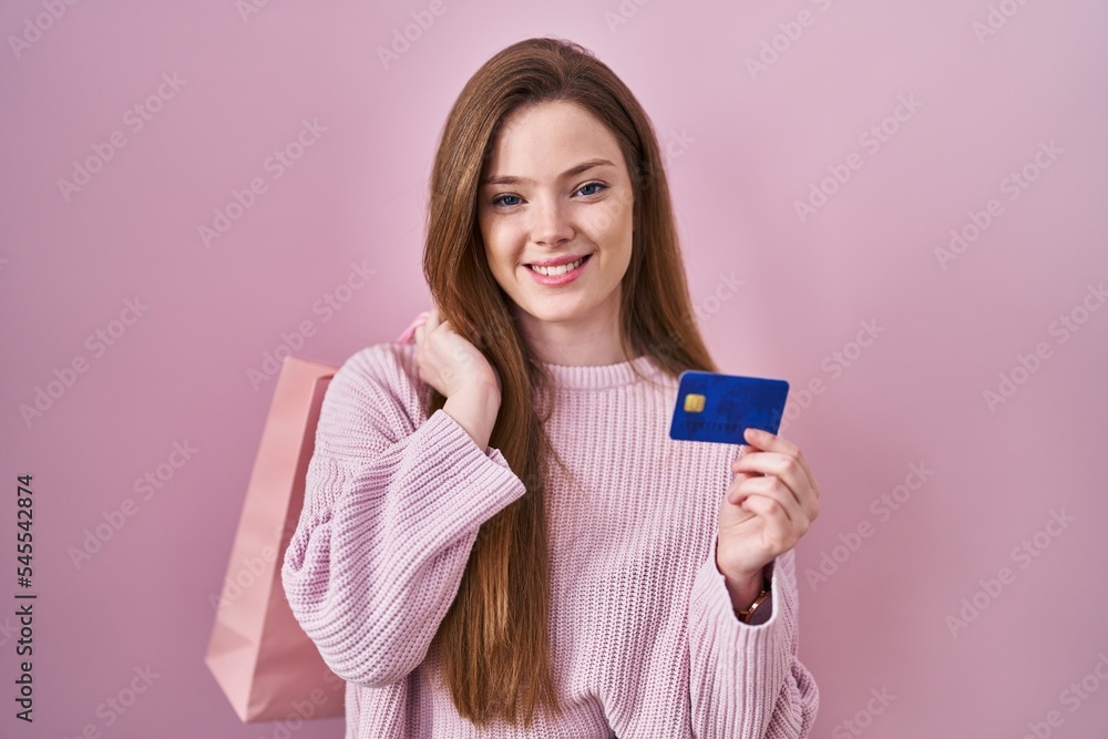 Young caucasian woman holding shopping bag and credit card smiling with a happy and cool smile on face. showing teeth. Young caucasian woman holding shopping bag and credit card smiling with a happy and cool smile on face. showing teeth.