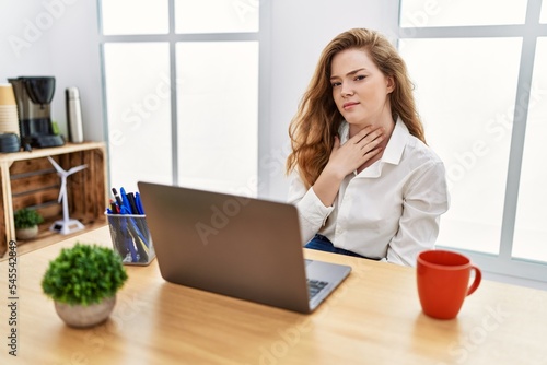 Young caucasian woman working at the office using computer laptop touching painful neck, sore throat for flu, clod and infection