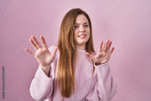 Young caucasian woman standing over pink background afraid and terrified with fear expression stop gesture with hands  shouting in shock. panic concept.