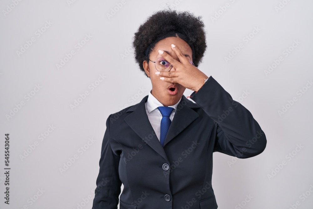 Beautiful african woman with curly hair wearing business jacket and glasses peeking in shock covering face and eyes with hand, looking through fingers with embarrassed expression. Beautiful african woman with curly hair wearing business jacket and glasses peeking in shock covering face and eyes with hand, looking through fingers with embarrassed expression.