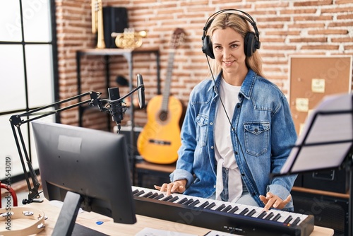 Young blonde woman musician playing piano keyboard at music studio