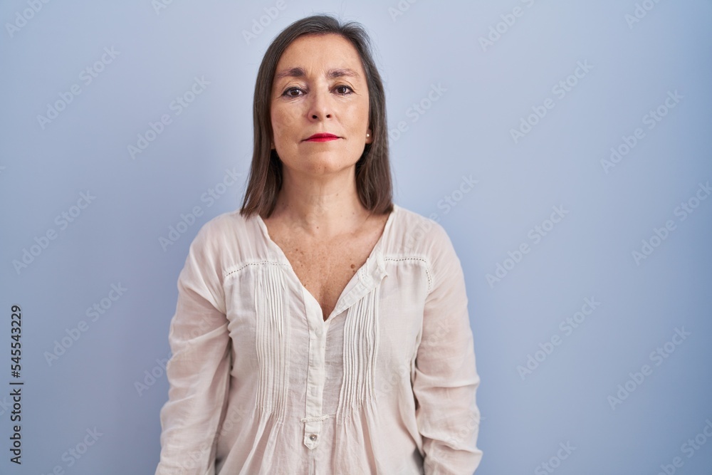 Middle age hispanic woman standing over blue background relaxed with serious expression on face. simple and natural looking at the camera. Middle age hispanic woman standing over blue background relaxed with serious expression on face. simple and natural looking at the camera.