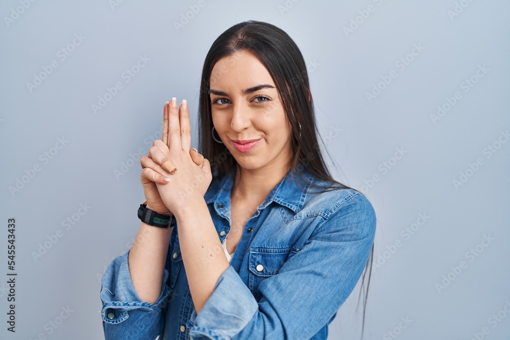 Hispanic woman standing over blue background holding symbolic gun with hand gesture, playing killing shooting weapons, angry face Hispanic woman standing over blue background holding symbolic gun with hand gesture, playing killing shooting weapons, angry face