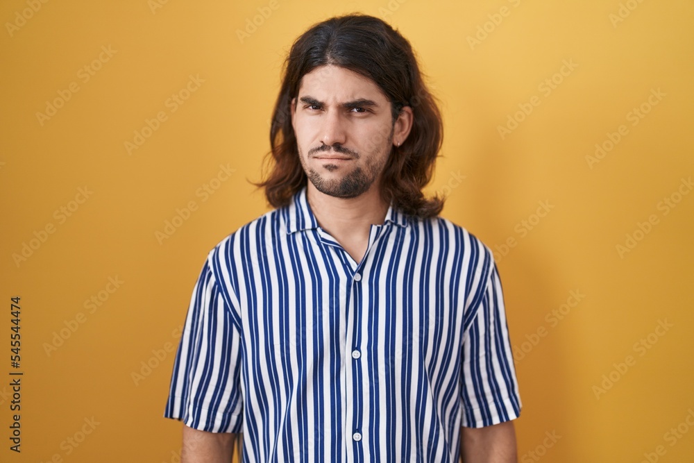 Hispanic man with long hair standing over yellow background skeptic and nervous, frowning upset because of problem. negative person. Hispanic man with long hair standing over yellow background skeptic and nervous, frowning upset because of problem. negative person.