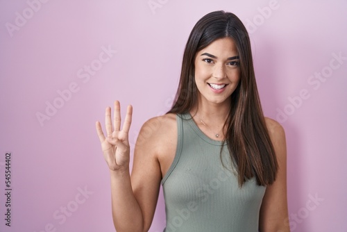 Hispanic woman standing over pink background showing and pointing up with fingers number four while smiling confident and happy.