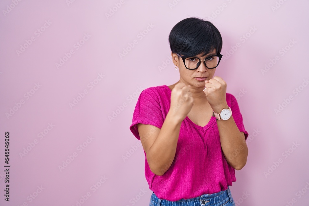 Young asian woman with short hair standing over pink background ready to fight with fist defense gesture, angry and upset face, afraid of problem Young asian woman with short hair standing over pink background ready to fight with fist defense gesture, angry and upset face, afraid of problem