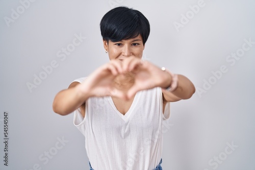 Young asian woman with short hair standing over isolated background smiling in love doing heart symbol shape with hands. romantic concept. © Krakenimages.com