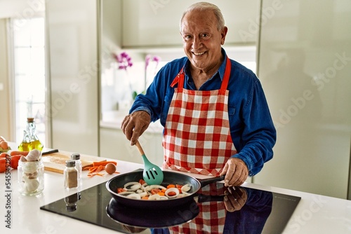 Senior man smiling confident cooking at kitchen