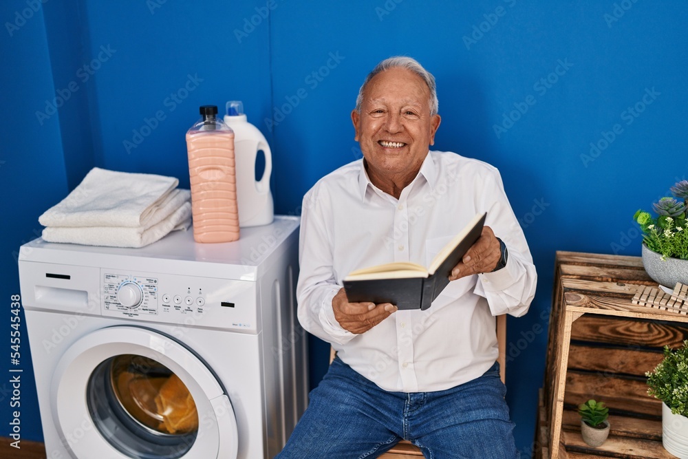 Senior man reading book waiting for washing machine at laundry room Senior man reading book waiting for washing machine at laundry room