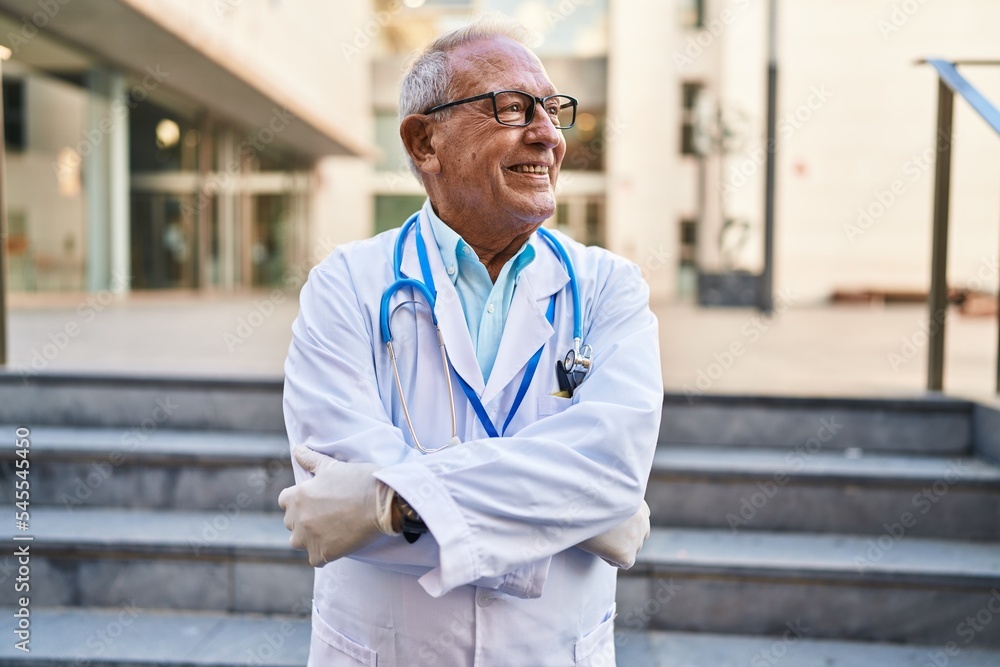 Φωτογραφία Senior man wearing doctor uniform standing with arms crossed gesture at street
