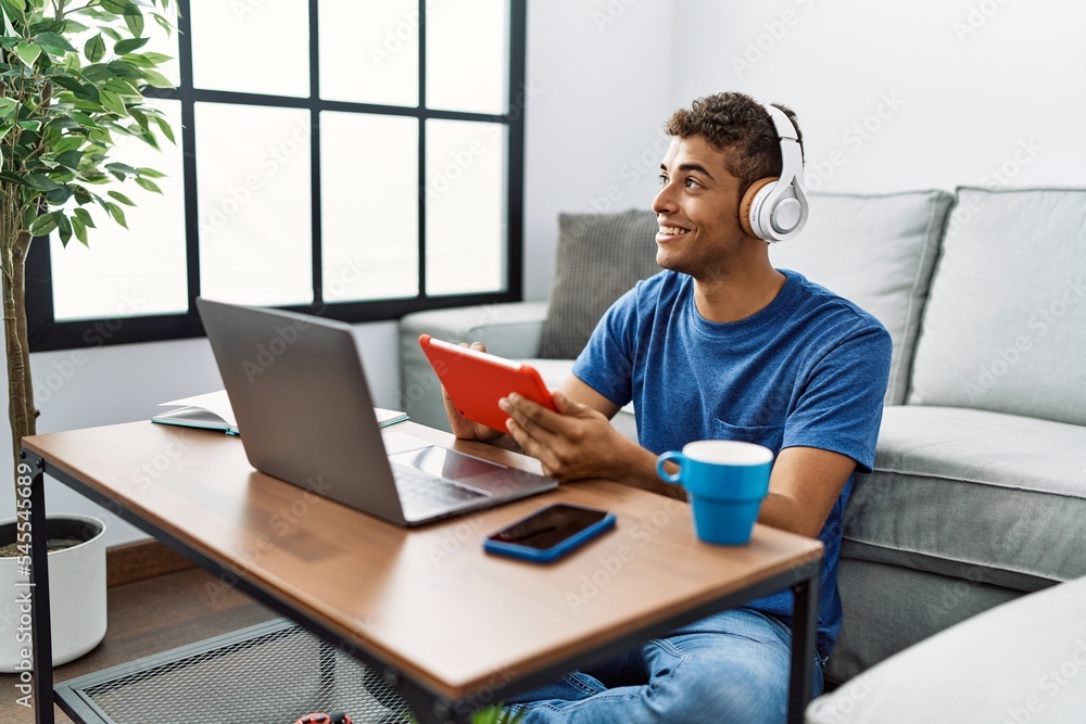 Young hispanic man using laptop and touchpad device at home Young hispanic man using laptop and touchpad device at home