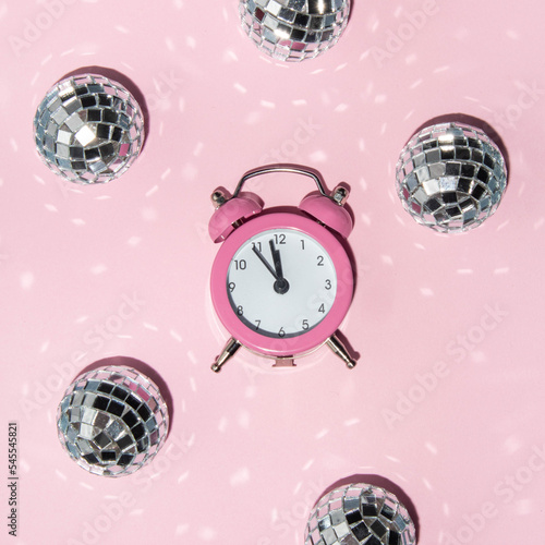Creative New Year party idea. Disco balls and clock on pastel light pink background. Minimalistic Christmas holidays idea. Trendy Xmas composition.