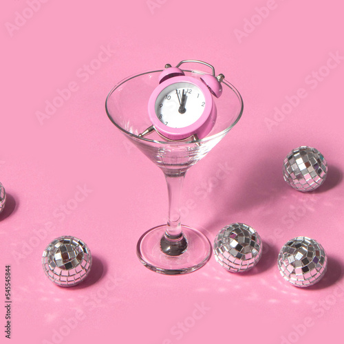 Creative New Year party idea. Disco balls and clock in cocktail glass on pastel light pink background. Minimalistic Christmas holidays idea. Trendy Xmas composition.