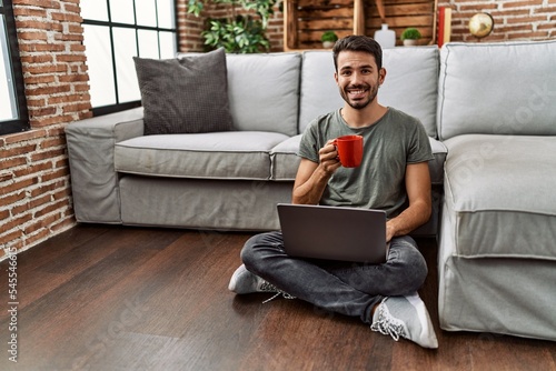Stampa su tela Young hispanic man using laptop and drinking coffee at home