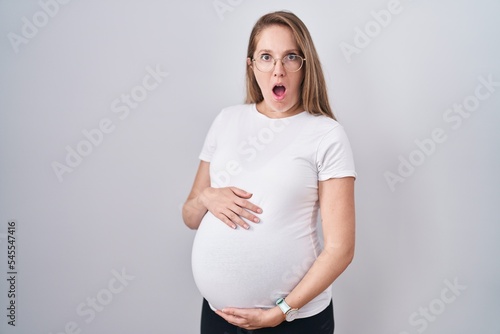 Young pregnant woman expecting a baby, touching pregnant belly afraid and shocked with surprise and amazed expression, fear and excited face.