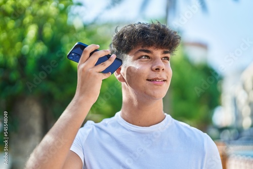 Young hispanic teenager smiling confident listening audio message by the smartphone at park