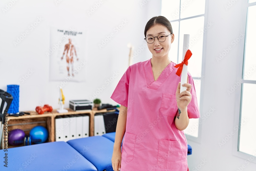 Young asian woman holding degree at physiotherapy clinic Young asian woman holding degree at physiotherapy clinic