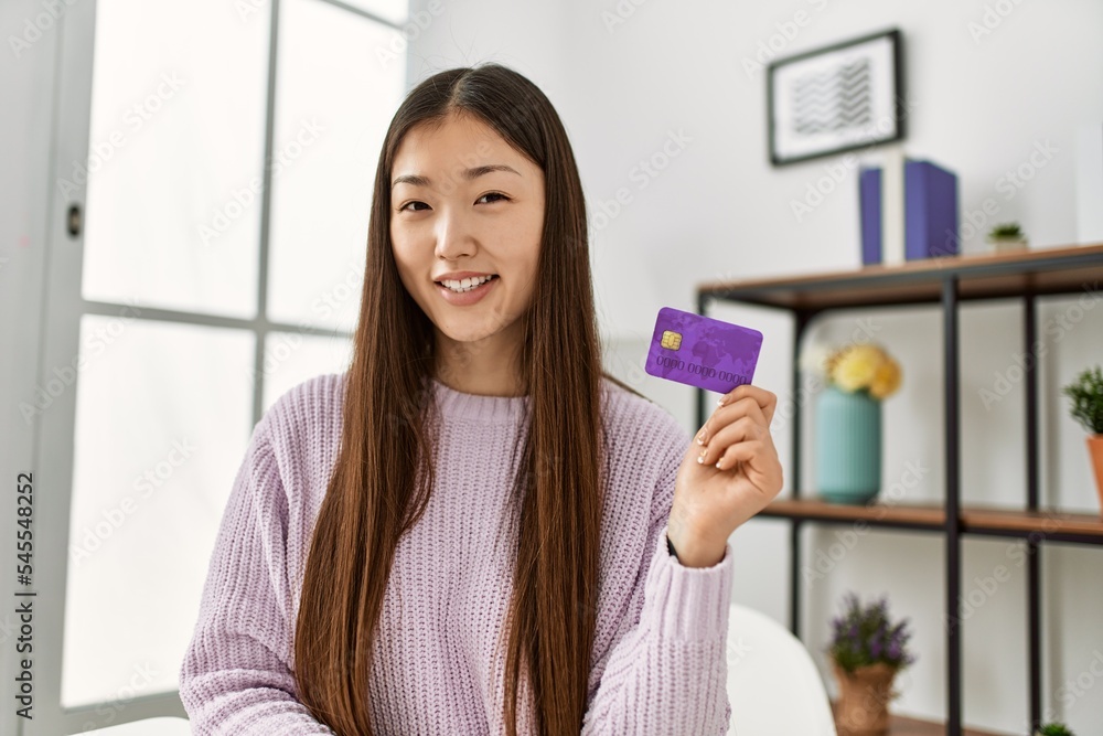 Young chinese girl holding credit card sitting on the table at home. Young chinese girl holding credit card sitting on the table at home.