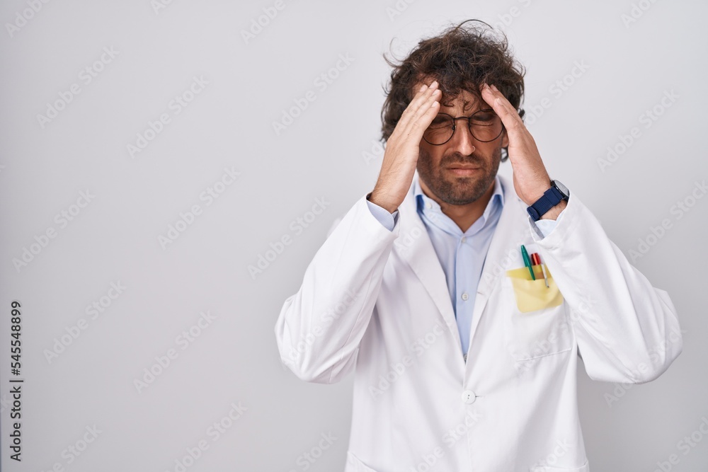 Hispanic young man wearing doctor uniform with hand on head for pain in head because stress. suffering migraine. Hispanic young man wearing doctor uniform with hand on head for pain in head because stress. suffering migraine.