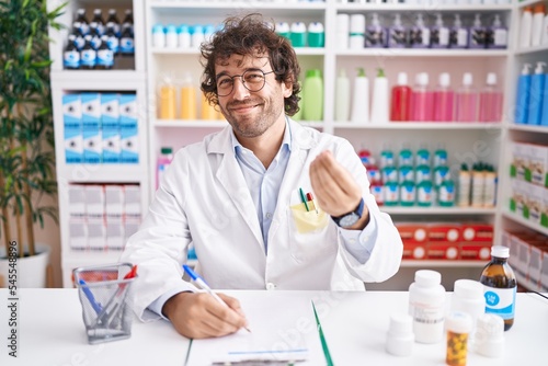 Hispanic young man working at pharmacy drugstore doing money gesture with hands, asking for salary payment, millionaire business