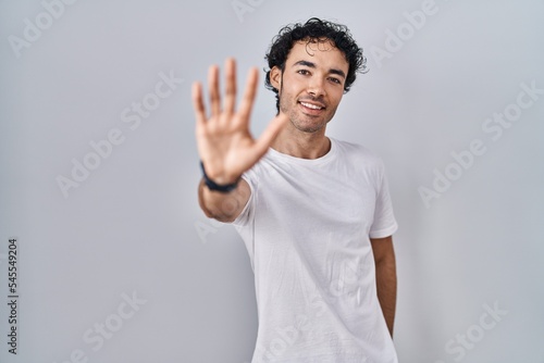 Hispanic man standing over isolated background showing and pointing up with fingers number five while smiling confident and happy.