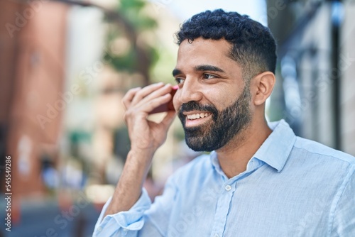 Young arab man miling confident listening audio message by the smartphone at street