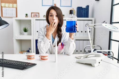 Young dentist woman holding mouthwash for fresh breath covering mouth with hand  shocked and afraid for mistake. surprised expression