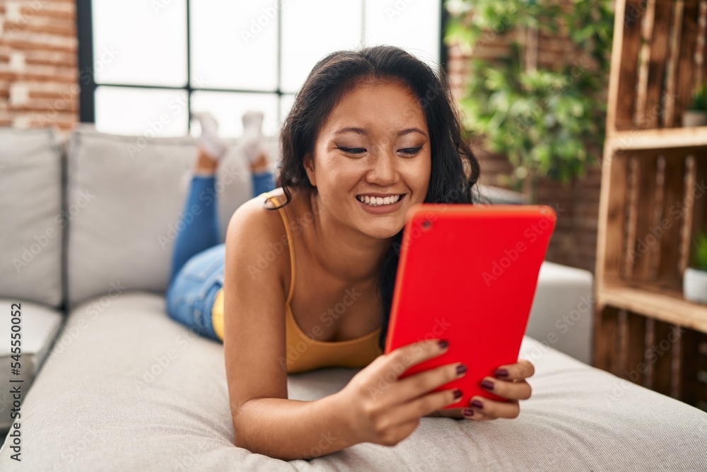 Young chinese woman using touchpad lying on sofa at home Young chinese woman using touchpad lying on sofa at home