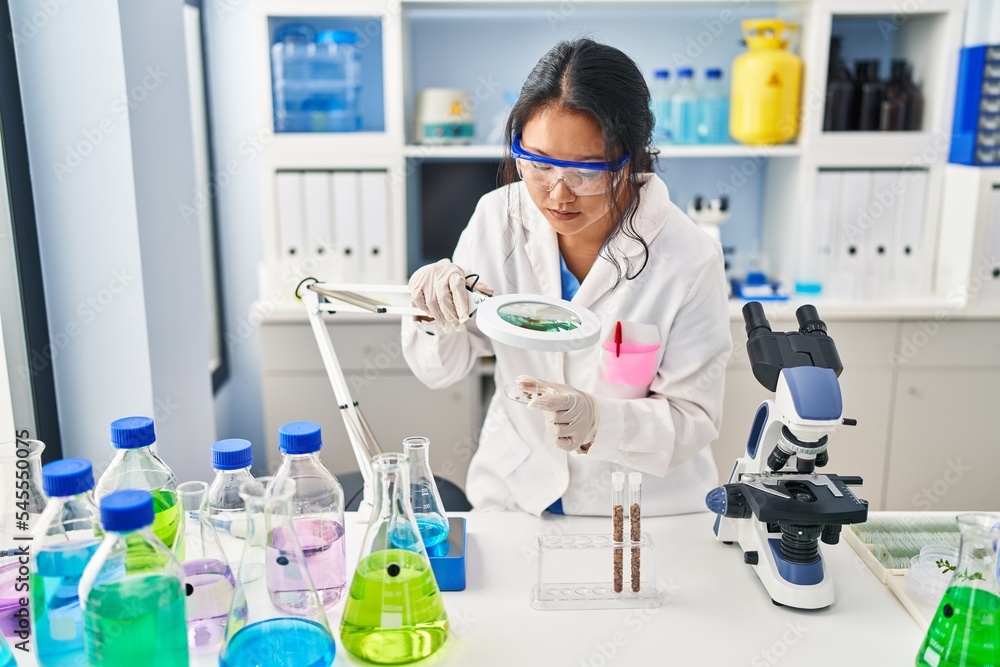 Young chinese woman wearing scientist uniform using loupe at laboratory Young chinese woman wearing scientist uniform using loupe at laboratory