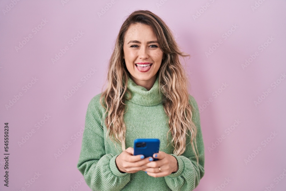 Young caucasian woman using smartphone typing message sticking tongue out happy with funny expression. Young caucasian woman using smartphone typing message sticking tongue out happy with funny expression.