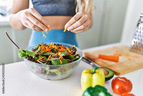 Young woman pouring carrot on salad at kitchen