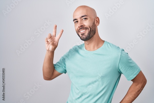 Middle age bald man standing over white background smiling looking to the camera showing fingers doing victory sign. number two.