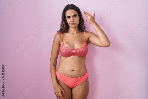 Young hispanic woman wearing lingerie over pink background shooting and killing oneself pointing hand and fingers to head like gun, suicide gesture.