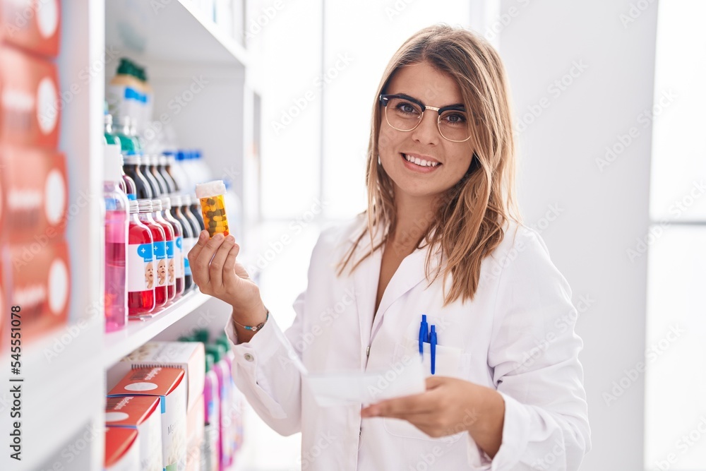 Young woman pharmacist holding pills bottle and prescription at pharmacy