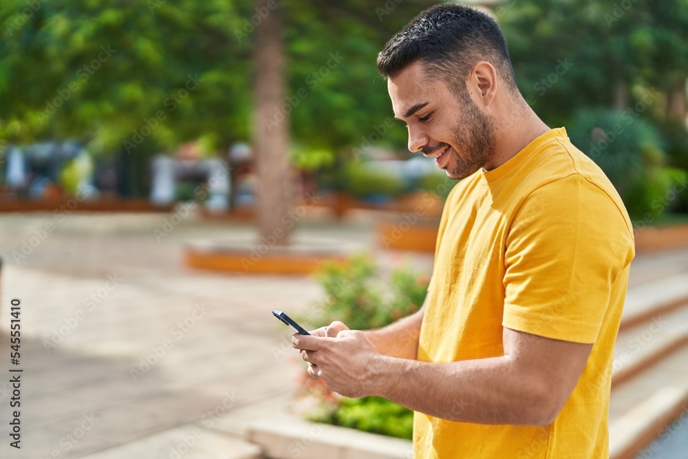 Fototapeta premium Young hispanic man smiling confident using smartphone at park