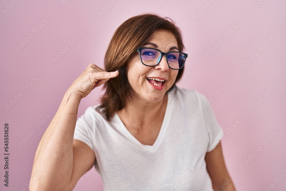 Middle age hispanic woman standing over pink background smiling doing phone gesture with hand and fingers like talking on the telephone. communicating concepts.