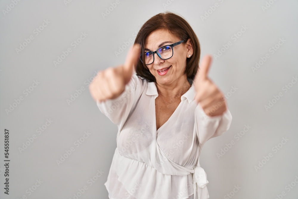 Middle age hispanic woman standing over isolated background approving doing positive gesture with hand, thumbs up smiling and happy for success. winner gesture. Middle age hispanic woman standing over isolated background approving doing positive gesture with hand, thumbs up smiling and happy for success. winner gesture.
