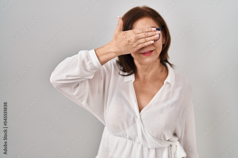 Middle age hispanic woman standing over isolated background smiling and laughing with hand on face covering eyes for surprise. blind concept. Middle age hispanic woman standing over isolated background smiling and laughing with hand on face covering eyes for surprise. blind concept.