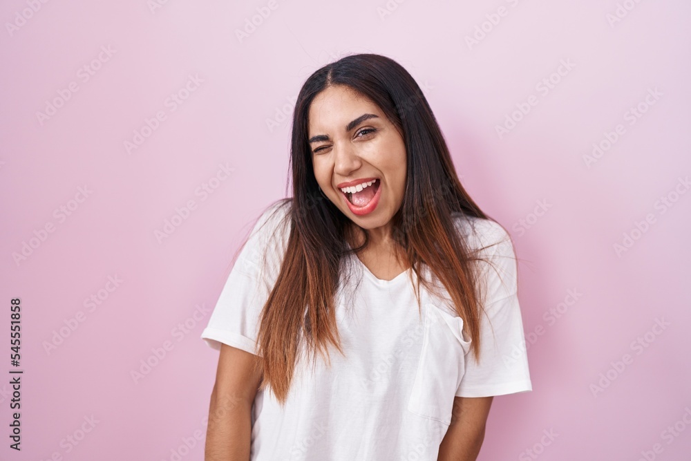Young arab woman standing over pink background winking looking at the camera with sexy expression, cheerful and happy face.