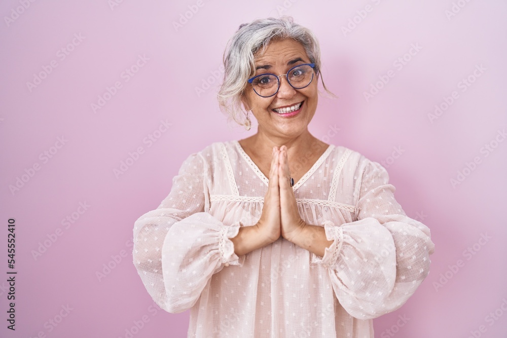 Middle age woman with grey hair standing over pink background praying with hands together asking for forgiveness smiling confident. Middle age woman with grey hair standing over pink background praying with hands together asking for forgiveness smiling confident.