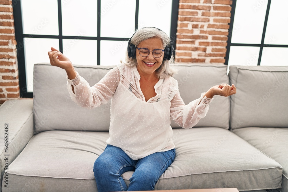 Fototapeta premium Middle age woman listening to music sitting on sofa at home