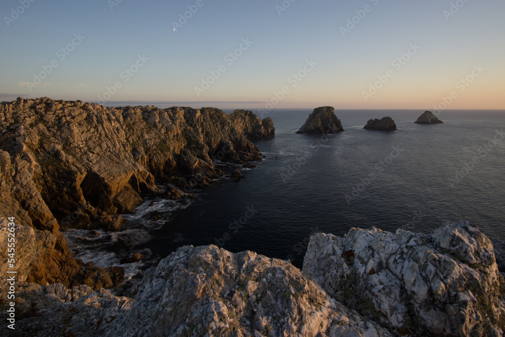 View at the coastline at Pointe de Pen-Hir at sunset with moon on the sky, Camaret-sur-Mer, Parc naturel regional Armorique, Brittany, France