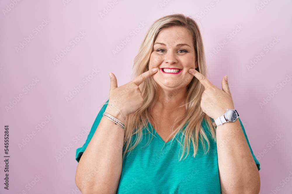 Caucasian plus size woman standing over pink background smiling with open mouth, fingers pointing and forcing cheerful smile Caucasian plus size woman standing over pink background smiling with open mouth, fingers pointing and forcing cheerful smile