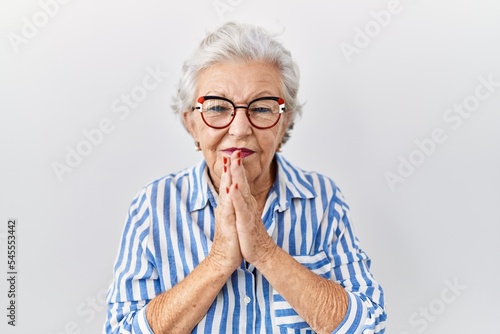 Senior woman with grey hair standing over white background begging and praying with hands together with hope expression on face very emotional and worried. begging.