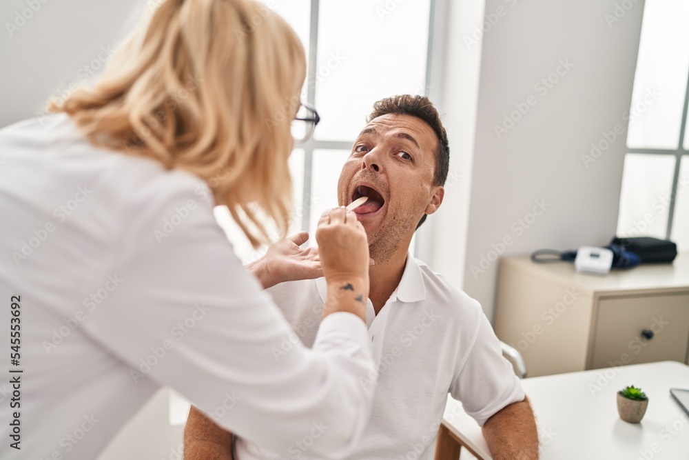 Middle age man and woman doctor and patient examining throat having medical consultation at clinic Middle age man and woman doctor and patient examining throat having medical consultation at clinic