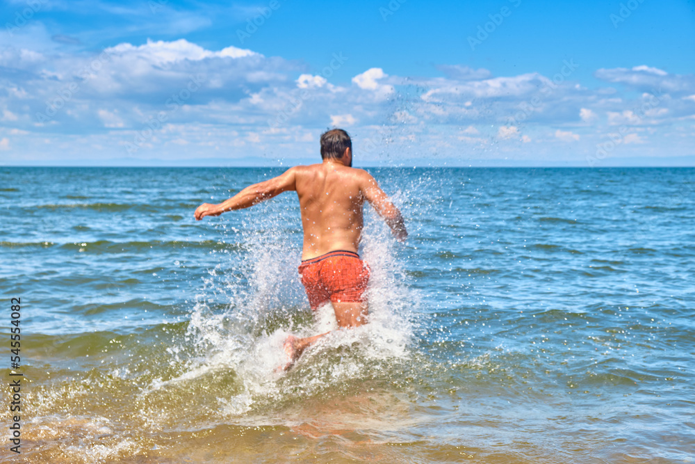 Fototapeta premium A young man runs into Lake Baikal. Siberia, Russia.