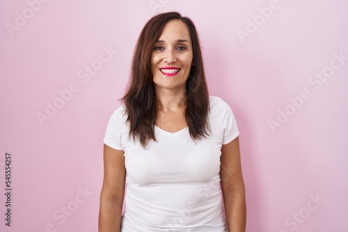Middle age brunette woman standing over pink background with a happy and cool smile on face. lucky person.