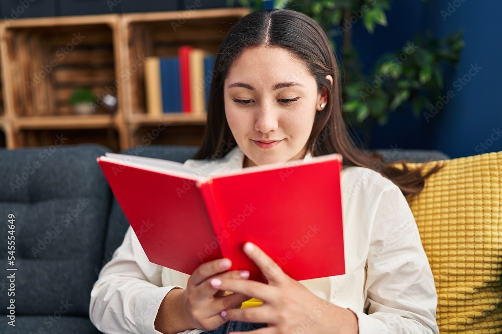 Young hispanic woman reading book sitting on sofa at home Young hispanic woman reading book sitting on sofa at home