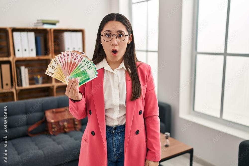 Young latin woman working at consultation office holding money scared and amazed with open mouth for surprise, disbelief face Young latin woman working at consultation office holding money scared and amazed with open mouth for surprise, disbelief face